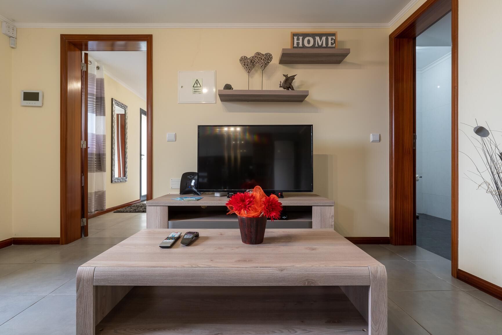 A living room with a television, a coffee table with a vase, and a 'HOME' sign on the wall.
