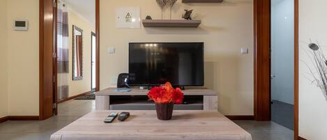 A living room with a television, a coffee table with a vase, and a 'HOME' sign on the wall.