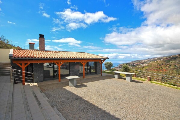 A covered outdoor seating area with a view of the sea and hills. - Gran Horizonte House (Ribeira Brava)
