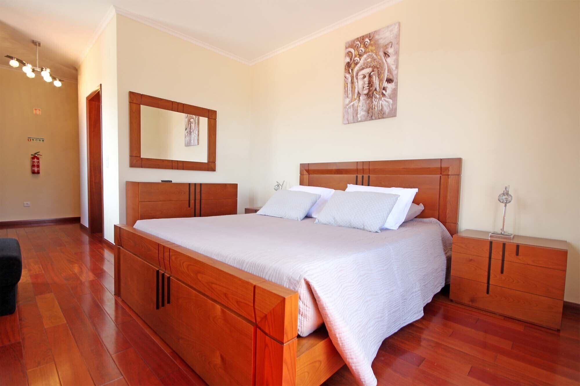 A bedroom with a wooden bed, a nightstand, a mirror, and a wall-mounted artwork.