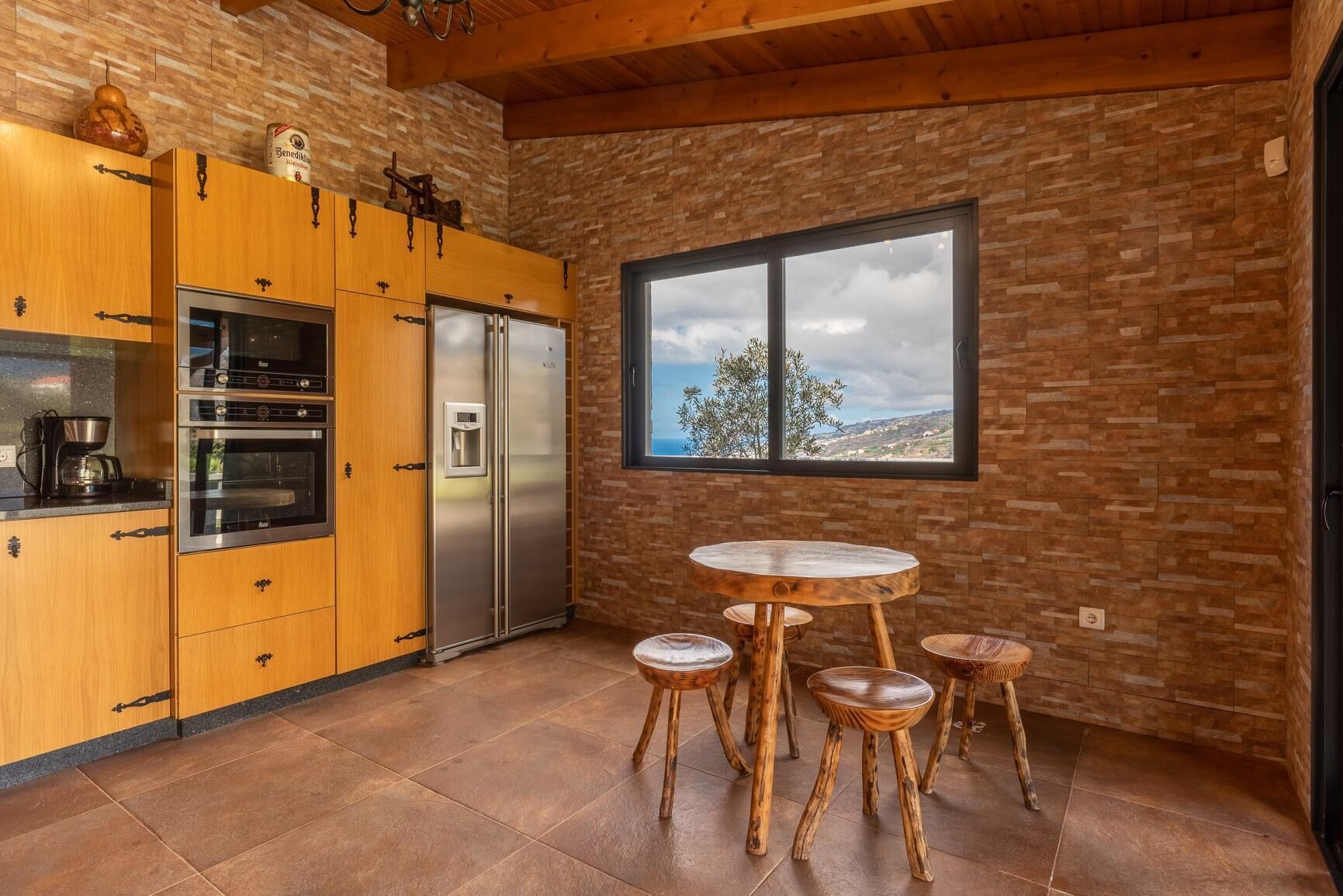 A kitchen with wooden cabinets, a stainless steel refrigerator, and a round wooden table with stools.