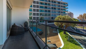 A balcony with outdoor seating, a swimming pool, and a view of a modern building. - Monumental Residence (Funchal)