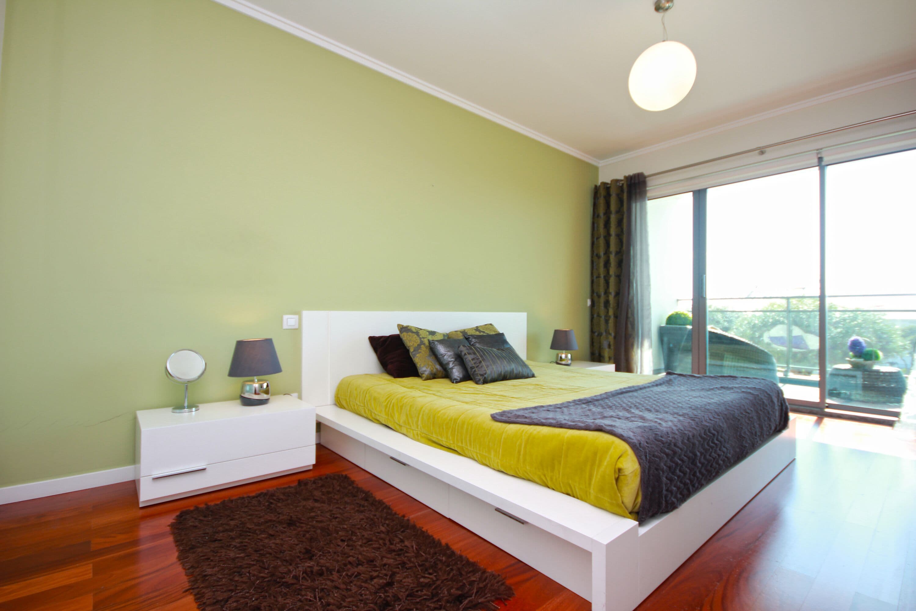 A bedroom with a bed, bedside tables, and a view of the outdoors.