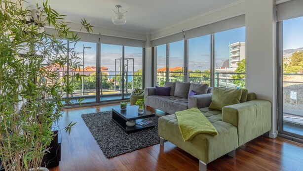 A modern living room with large windows, a grey sofa, a green armchair, and a black coffee table. - Monumental Residence (Funchal)