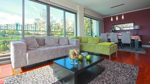A modern living room with a sofa, a coffee table with decorative items, and a dining area with a table and chairs. - Monumental Residence (Funchal)