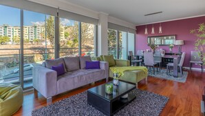 A modern living room with a large window, a sofa, a coffee table, and a dining area with chairs and a table. - Monumental Residence (Funchal)