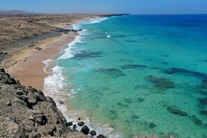 A coastal landscape with clear turquoise waters, rocky terrain, and a distant mountain range. - Beach Apartment Marfolin 06 El Cotillo (La Oliva)