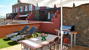 Une terrasse extérieure avec une table et des chaises, un barbecue et, au fond, un espace piscine.