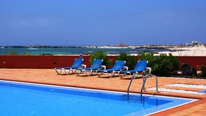 A poolside area with blue lounge chairs and a clear view of the beach and ocean.