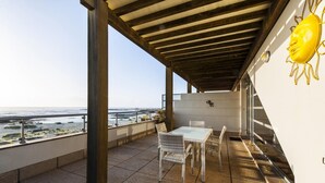 A covered outdoor patio with a table and chairs, overlooking a coastal view.