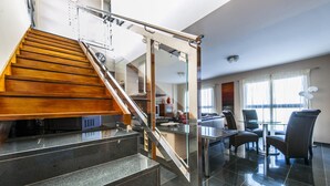 A modern interior with a wooden staircase, a glass dining area, and a kitchen in the background.