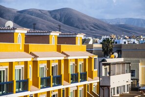 A row of yellow buildings with multiple windows and balconies, set against a mountainous backdrop. - Beach Apartment Marfolin 19 El Cotillo (La Oliva)
