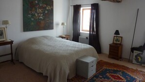 Un dormitorio con una cama grande, un cuadro, una ventana con cortinas, una mesita de noche, una lámpara y una alfombra.