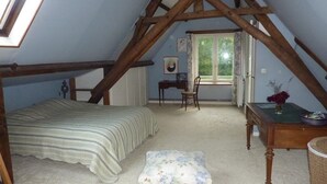 Un dormitorio con techo inclinado, una cama, una silla, una mesita y una ventana.
