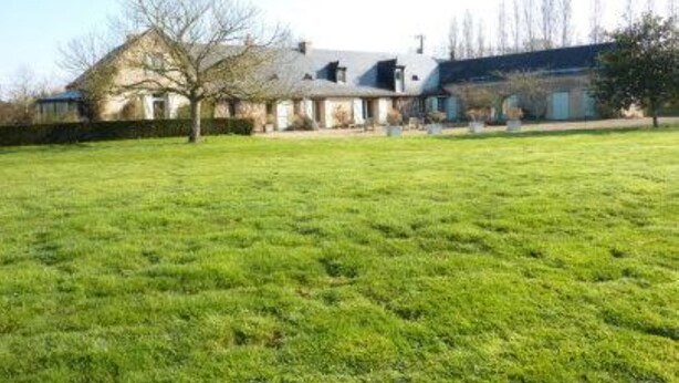 Un extenso campo cubierto de césped con una casa al fondo.