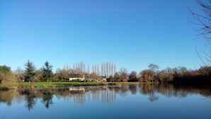 Un lago tranquilo con un reflejo claro, rodeado de árboles y un edificio a lo lejos.