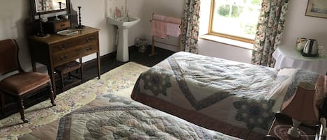 Een slaapkamer met twee bedden, een kaptafel, een spiegel, een wastafel en een raam met gordijnen.