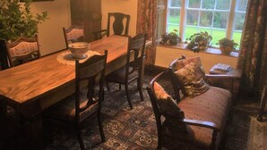 A dining area with a wooden table, chairs, a bowl on the table, and a window with plants outside. - Powter Howe (Keswick)