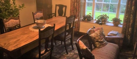 Un coin repas avec une table en bois, des chaises, un bol posé sur la table et une fenêtre donnant sur des plantes à l’extérieur.