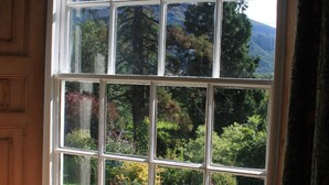 A large window with multiple panes, offering a view of a lush garden and tall trees. - Powter Howe (Keswick)