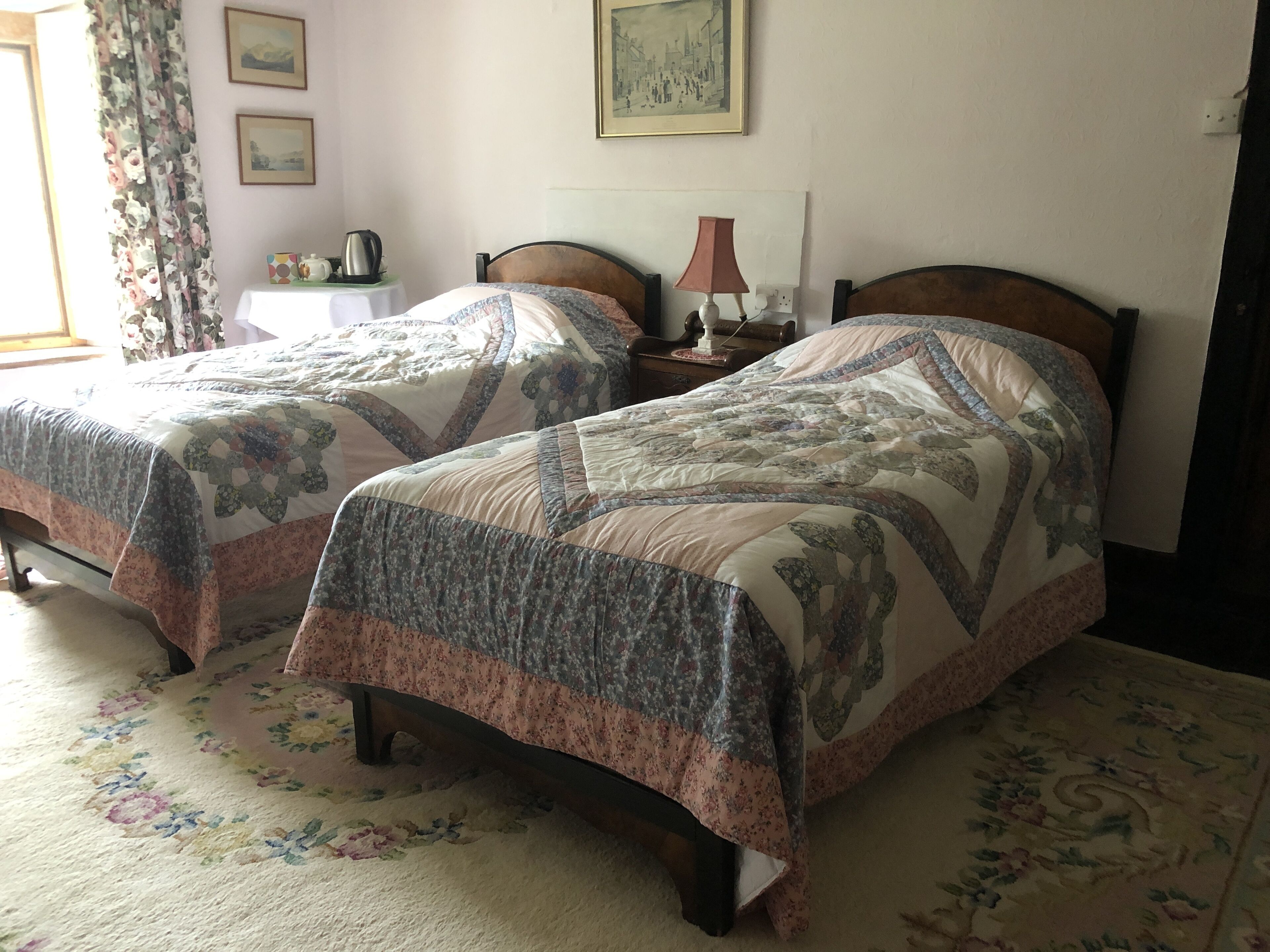 Une chambre avec deux lits, chacun agrémenté de draps à motifs floraux, une table de chevet avec une lampe et un tableau au mur.