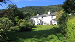 A white house with a well-maintained lawn and a forested hill in the background. - Powter Howe (Keswick)