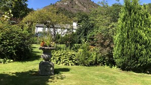 A garden with a white building, a mountain in the background, and a stone urn in the foreground. - Powter Howe (Keswick)