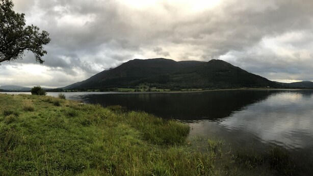 A calm lake with mountains in the background and overcast sky. - Powter Howe (Keswick)