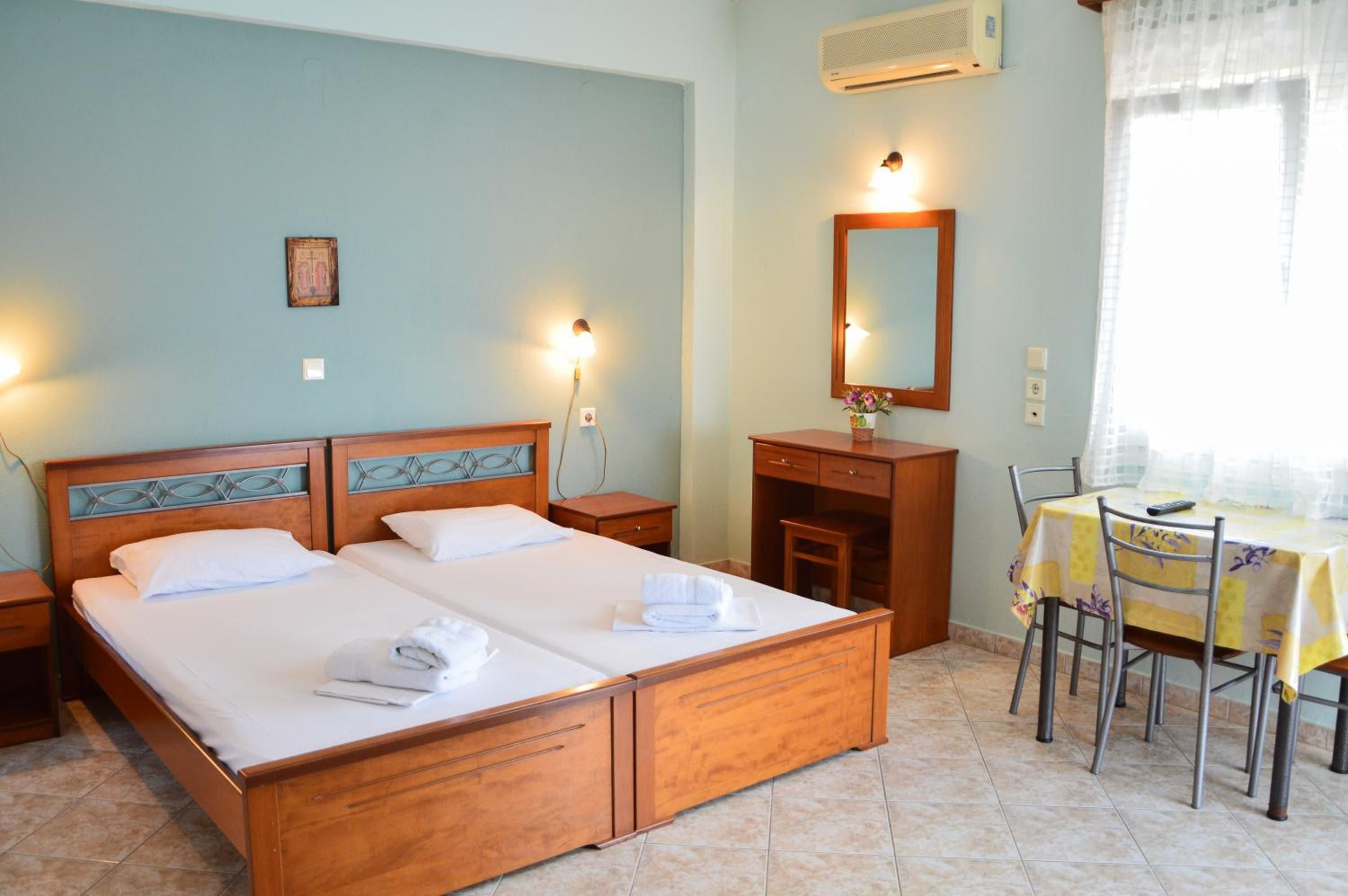 A hotel room with a double bed, a desk with a chair, a mirror, and a window with curtains.