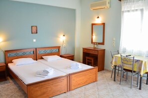 A hotel room with a double bed, a desk with a chair, a mirror, and a window with curtains.