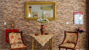 A room with a brick wall, a gold-framed mirror, two upholstered chairs, a small table with a vase of flowers, and a red cabinet. - Vergina (Thasos)