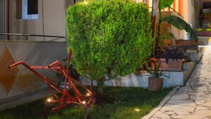 A well-maintained garden with a neatly trimmed bush, a potted plant, and a metal structure with lights. - Vergina (Thasos)