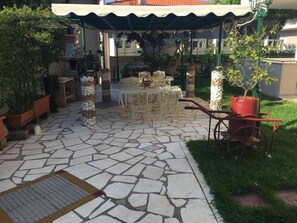 An outdoor patio area with a stone floor, outdoor furniture, and potted plants.