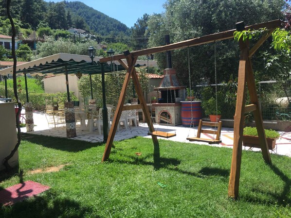 A patio area with a swing set, outdoor seating, and a barbecue grill.