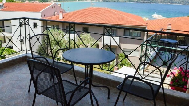 A balcony with a table and chairs, overlooking a coastal view with mountains in the background. - Vergina (Thasos)