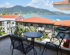 A balcony with a table and chairs, overlooking a coastal view with mountains in the background.
