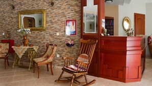 A lobby with a brick wall, a reception desk, a mirror, and a chair. - Vergina (Thasos)