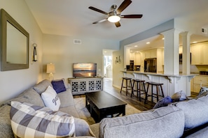 A modern living room with a sofa, a coffee table, and a TV. There is a kitchen area with a refrigerator and bar stools. - 1109 Harbour South - Perfect Island Retreat (Hilton Head Island)