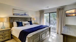 Ein Schlafzimmer mit einem großen Bett, einem Nachttisch, einem Schreibtisch, einem Fernseher und einem Fenster mit Vorhängen.