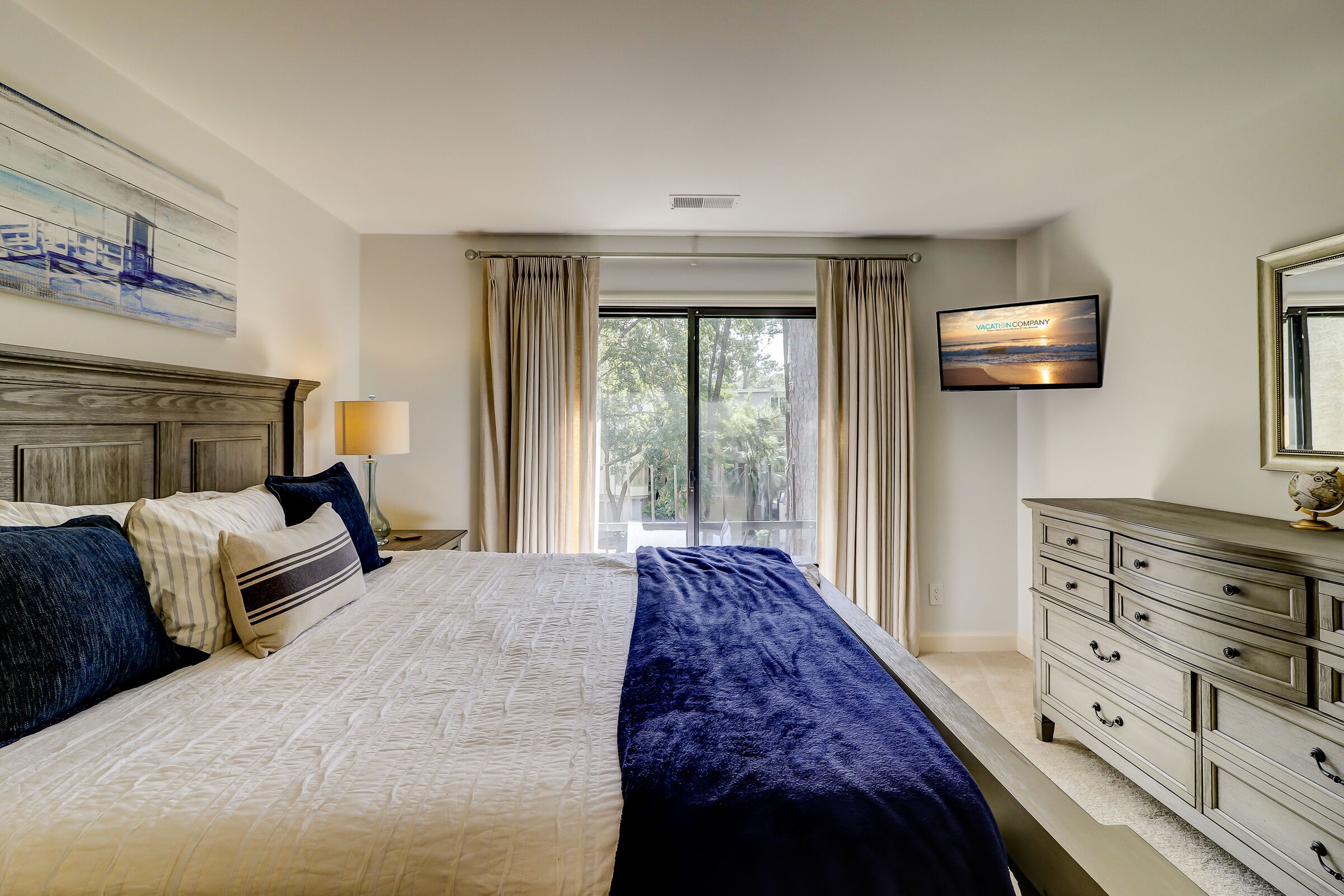 Une chambre à coucher avec un grand lit, une commode, un téléviseur et une fenêtre avec des rideaux.