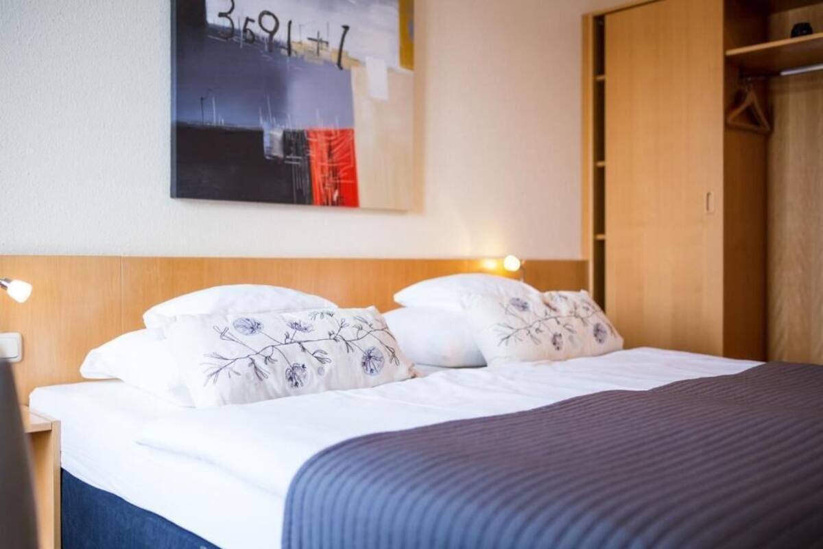 Ein ordentlich bezogenes Bett mit blumigen Kissen, einem Holzkopfstück und einem an der Wand hängenden Kunstwerk.