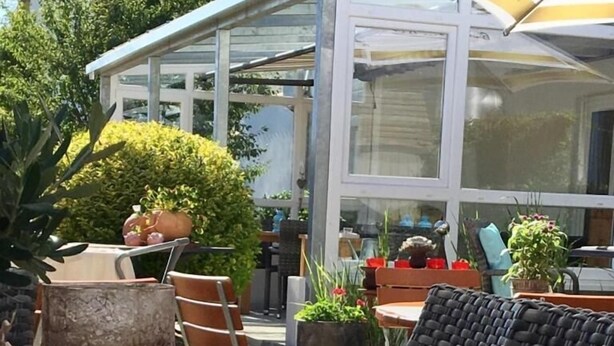 An outdoor seating area with a table set for two, featuring a glass candle holder, a menu, and a wicker chair. - Hotel am Kellhof (Hilzingen)