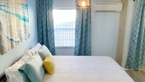 A neatly made bed with pillows, a window with blinds, and patterned curtains. - An oasis ACROSS THE STREET FROM THE BEACH :) (Treasure Island)