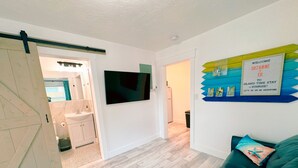 A modern living room with a teal sofa, a mounted flat-screen TV, and a welcome sign. - An oasis ACROSS THE STREET FROM THE BEACH :) (Treasure Island)