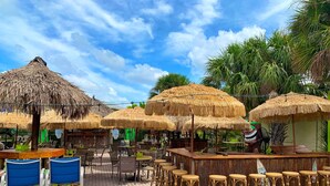 A beachside restaurant with thatched umbrellas, wicker bar stools, and outdoor seating. - An oasis ACROSS THE STREET FROM THE BEACH :) (Treasure Island)