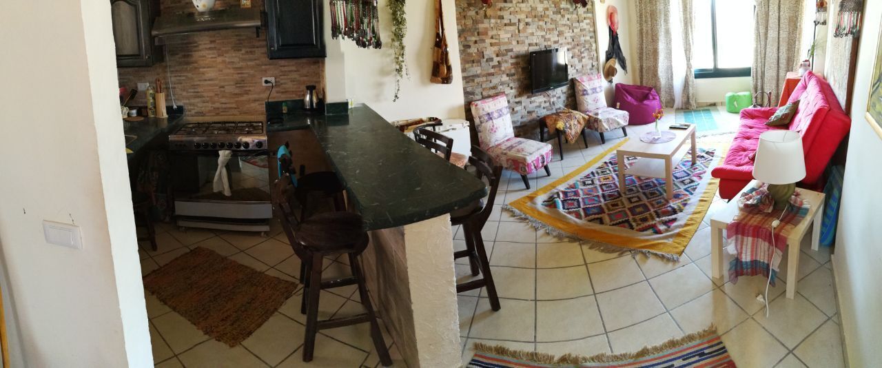 A kitchen with a stove, a dining table with chairs, a living area with a sofa and a TV, and a patterned rug.