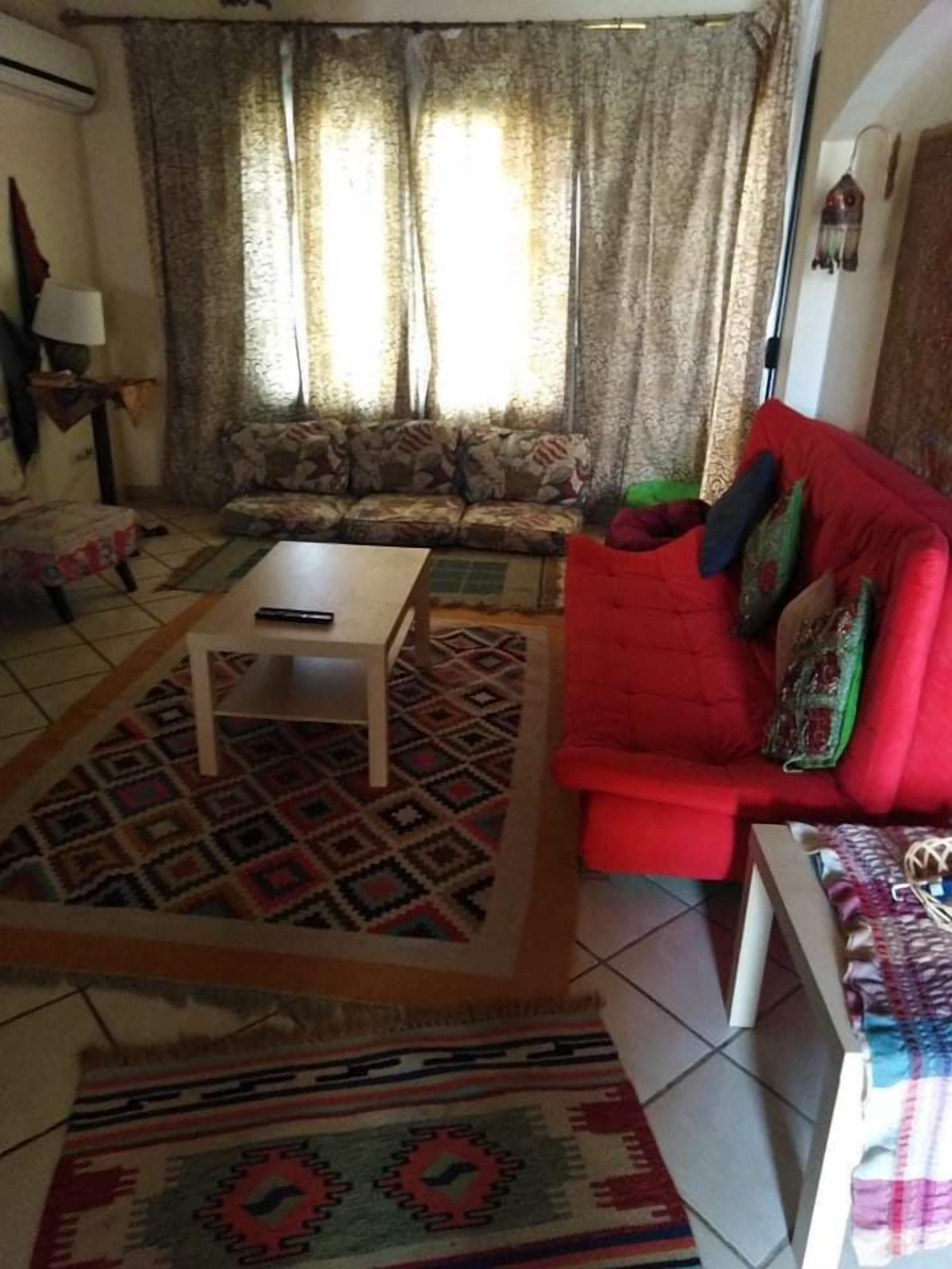A living room with a patterned rug, a red sofa, a wooden coffee table, and a patterned rug on the floor.