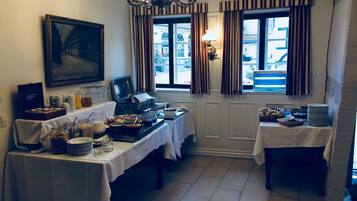 Un bufé de desayuno con diversas opciones de comida y una estación de café, ubicado en una habitación con un amplio ventanal y cortinas.