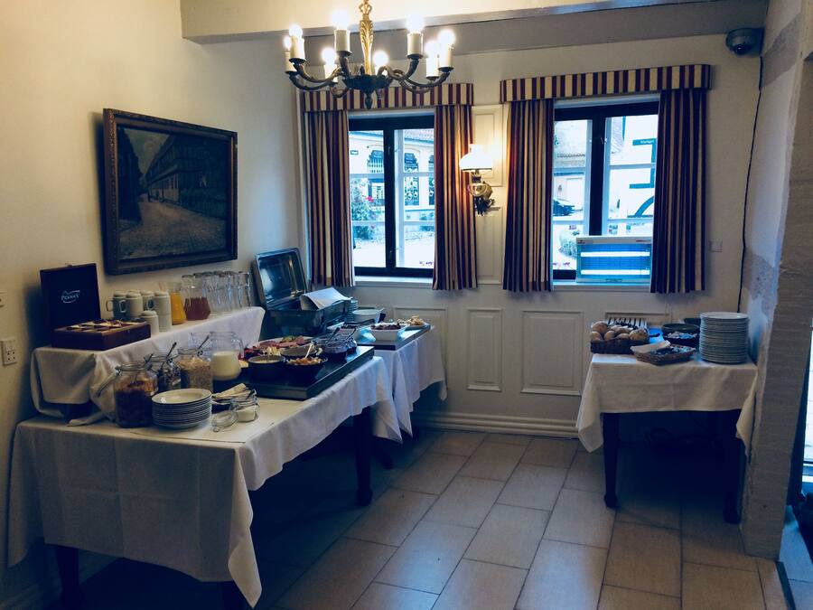 Un bufé de desayuno con diversas opciones de comida y una estación de café, ubicado en una habitación con un amplio ventanal y cortinas.