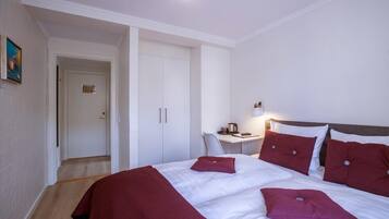 A hotel room with a bed, a desk, and a chair. There is a door leading to another room.